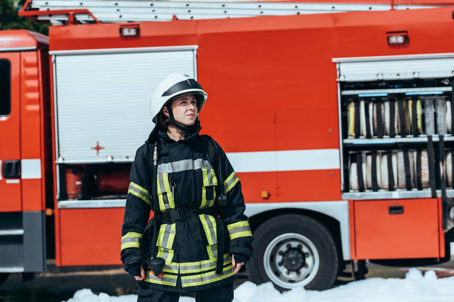 Female firefighter standing in front of a firetruck in full uniform.
